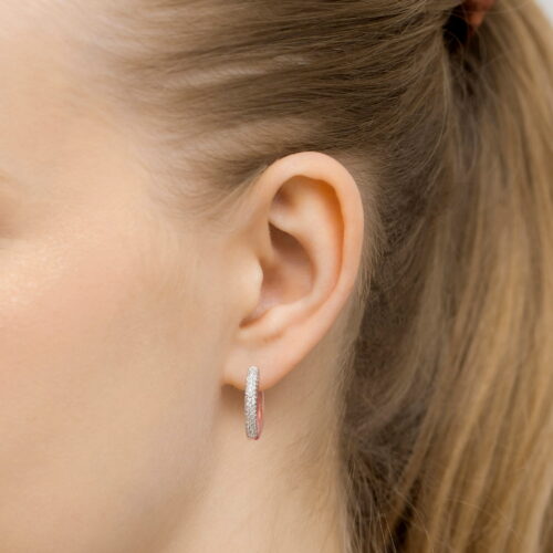 Kobieta z długimi włosami nosi srebrne kolczyki w kształcie obręczy.