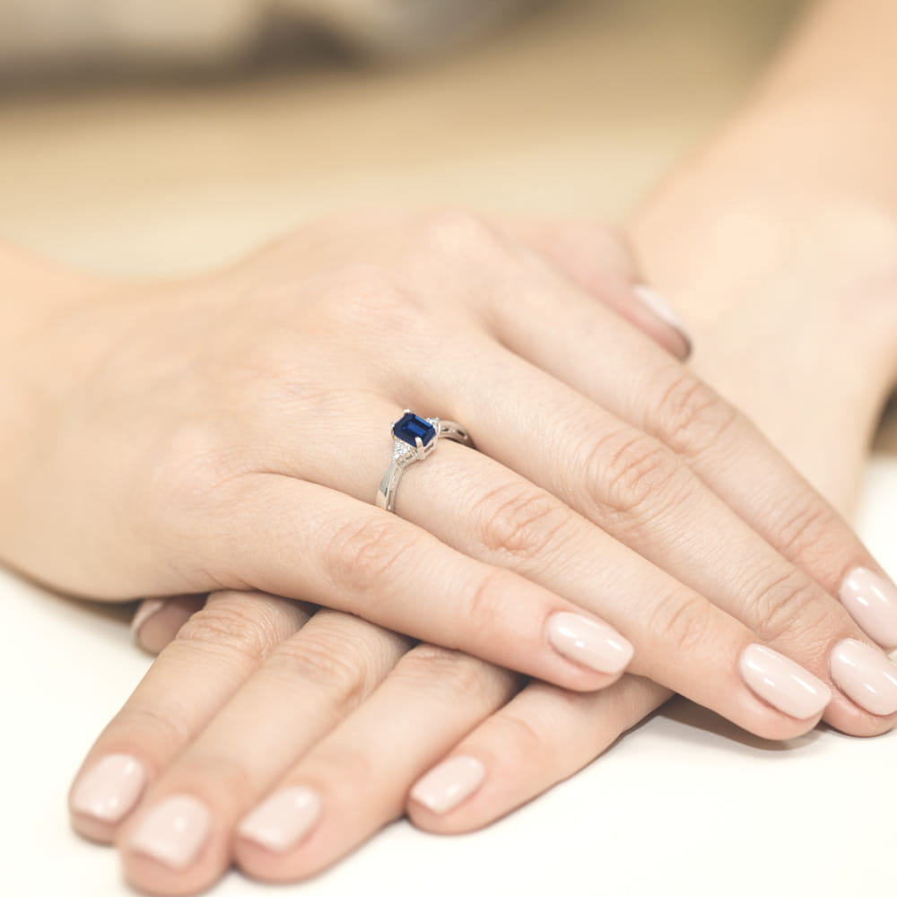 W0002.B3.SAB.01_4 Na dłoniach z delikatnym manicure znajduje się srebrny pierścionek z niebieskim kamieniem.