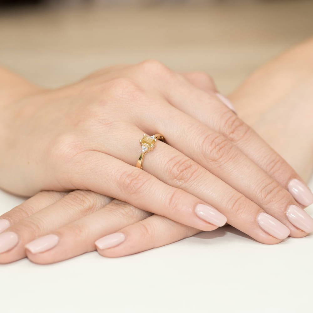 W0002.Z3.CIY.01_4 Złoty pierścionek z diamentem na palcu, dłonie z delikatnym manicure w jasnym kolorze.