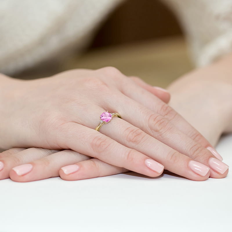 W0003.Z3.TOP.01_4 Na dłoniach z delikatnym manicure znajduje się złoty pierścionek z różowym kamieniem.