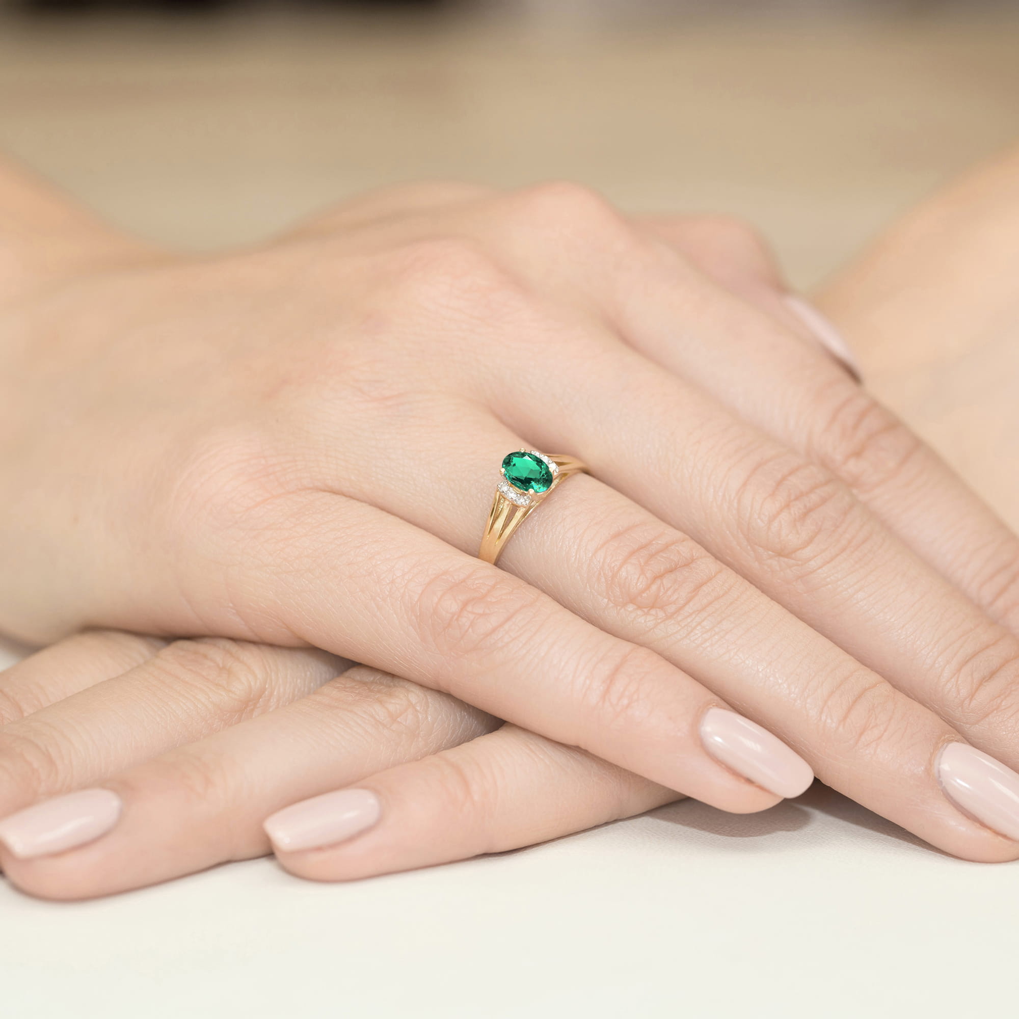 W0005.Z3.EMG.01_4 Złoty pierścionek z zielonym kamieniem na palcu, dłonie z delikatnym manicure w jasnym kolorze.