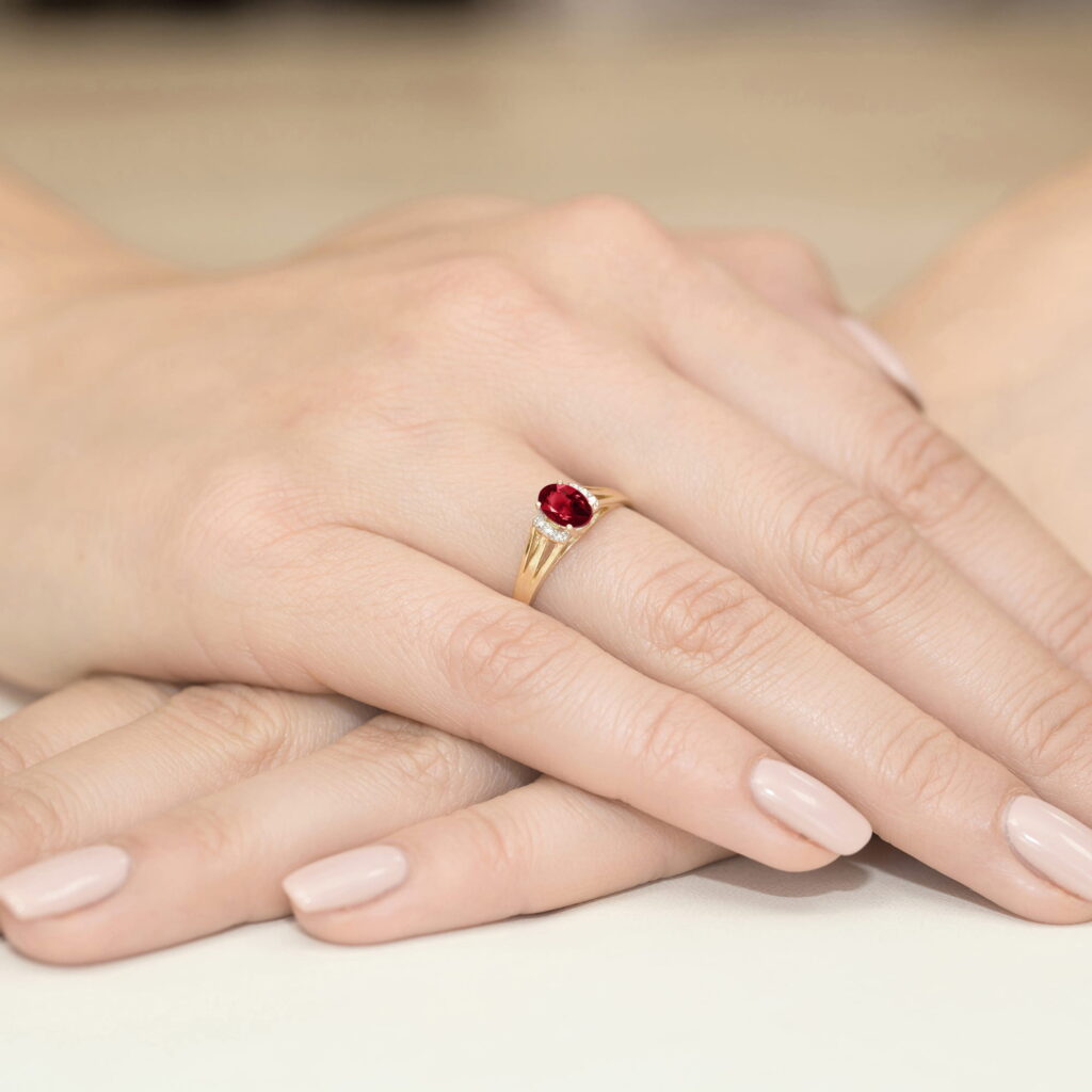 Złoty pierścionek z czerwonym kamieniem na palcu, dłonie z delikatnym manicure w jasnym kolorze.