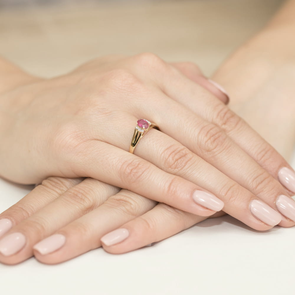 W0005.Z3.RUR.01_4 Złoty pierścionek z różowym kamieniem na palcu, dłonie z delikatnym manicure w jasnym kolorze.