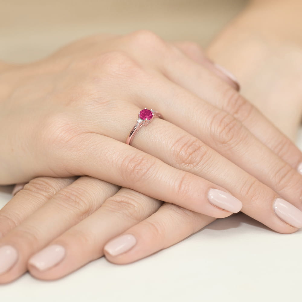 W0010.R3.RUR.01_4 Ręka z różowym pierścionkiem na palcu, otoczona dłońmi z zadbanymi paznokciami w jasnym kolorze.