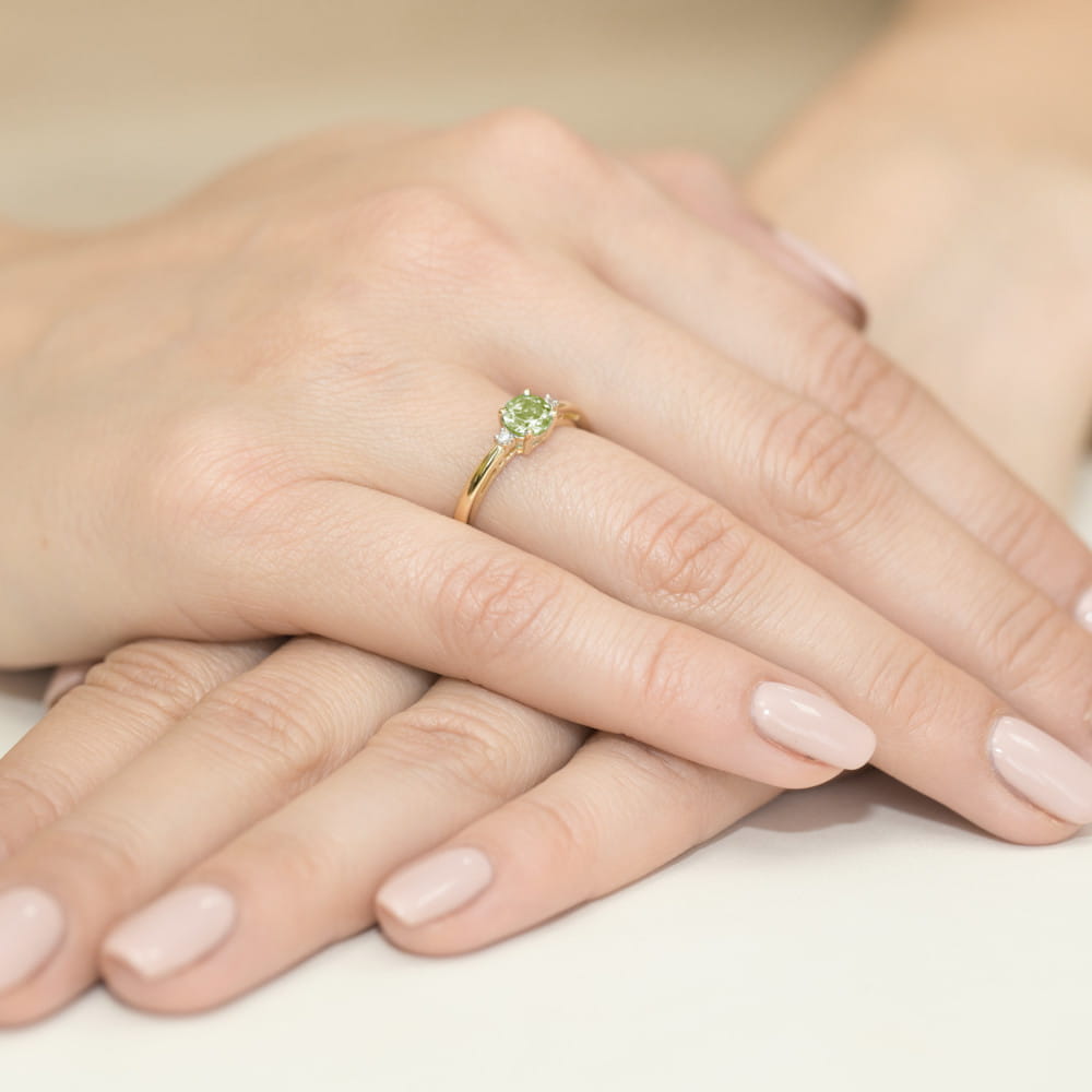 W0010.Z3.PEG.01_4 Złoty pierścionek z zielonym kamieniem na palcu, dłonie z delikatnym manicure w jasnym kolorze.