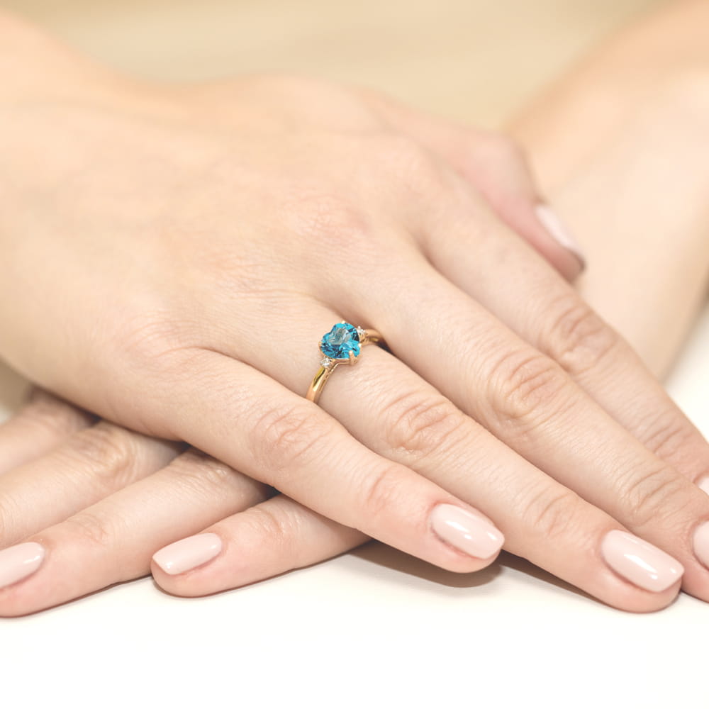 W0012.Z3.TOB.01_4 Złoty pierścionek z niebieskim kamieniem na palcu, dłonie z zadbanymi paznokciami.