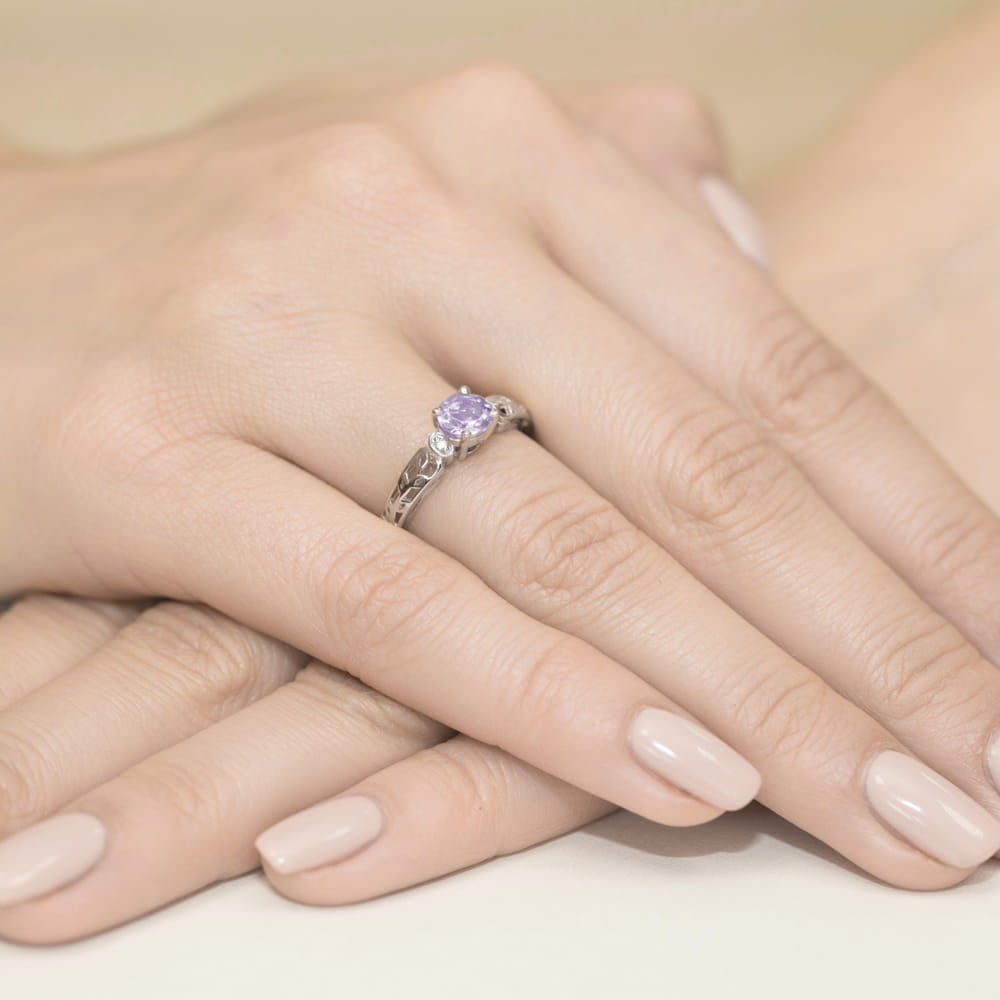 W0014.B3.AMV.01_4 Na dłoni widać srebrny pierścionek z fioletowym kamieniem i delikatnym wzorem, otoczony zadbanymi paznokciami.