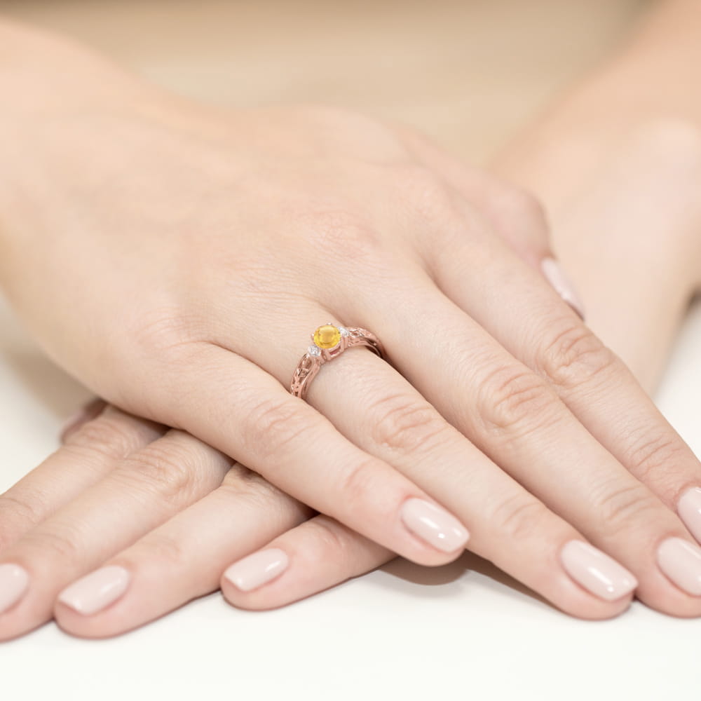 W0014.R3.CIY.01_4 Na dłoni widać pierścionek z żółtym kamieniem, otoczony delikatnym, złotym wzorem.