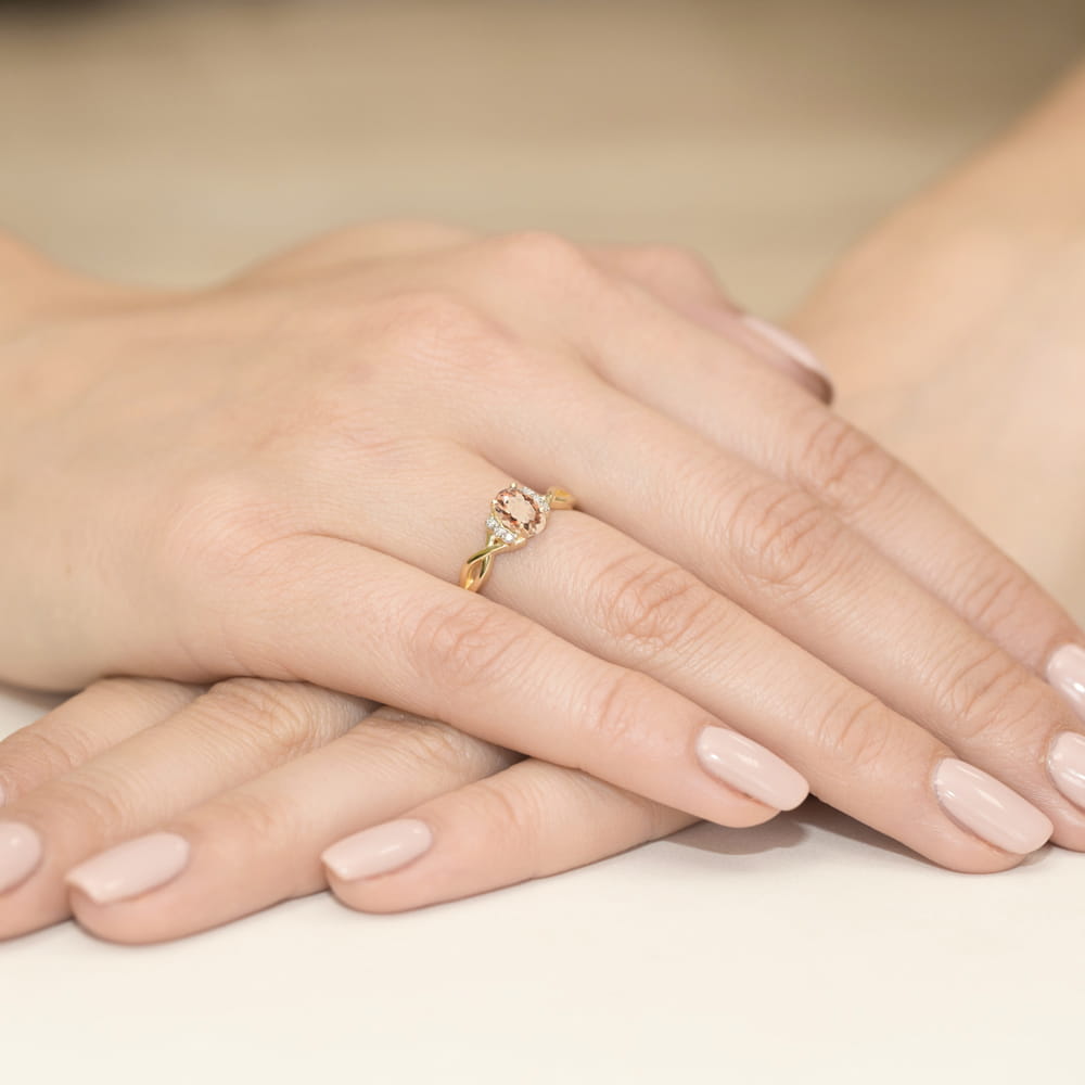 W0019.Z3.MOP.01_4 Złoty pierścionek z różowym kamieniem na palcu, dłonie z delikatnym manicure w jasnym kolorze.