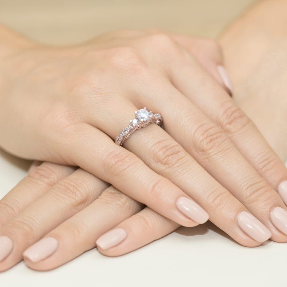 W0023.R3.SAW.01_4 Na dłoni z delikatnym manicure znajduje się pierścionek z dużym diamentem i ozdobnymi detalami.