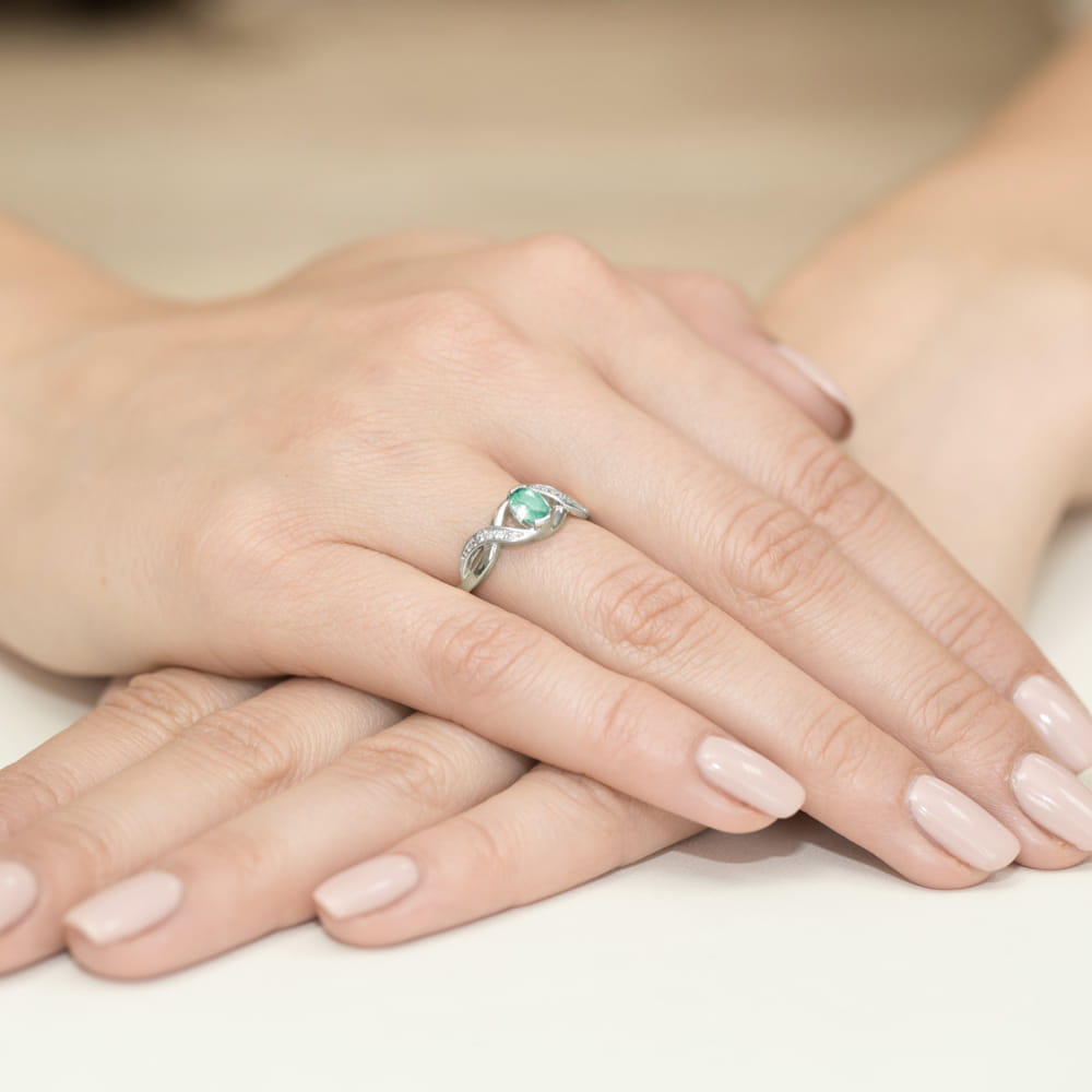 W0028.B3.EMG.01_4 Srebrny pierścionek z zielonym kamieniem na palcu, dłonie z delikatnym manicure w jasnym kolorze.