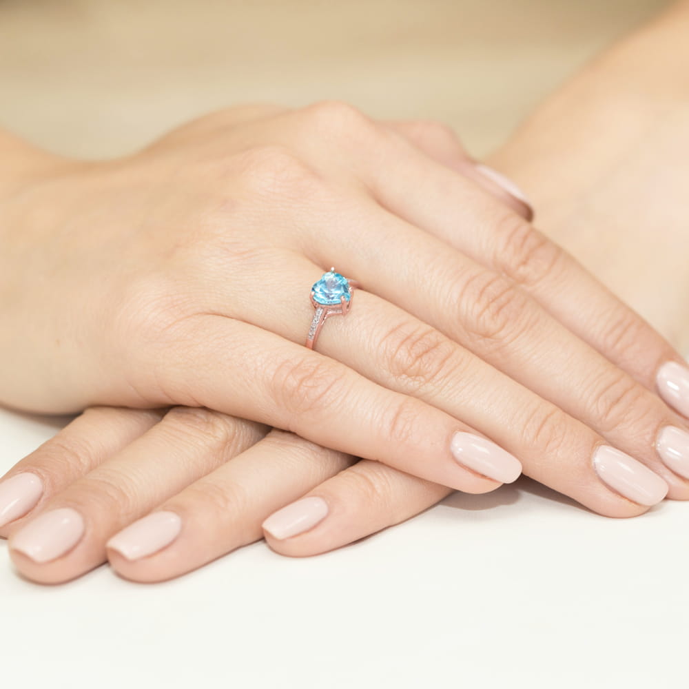 W0031.R3.TOB.01_4 Dwie dłonie z delikatnym manicure, na jednej z nich błyszczący pierścionek z niebieskim kamieniem.