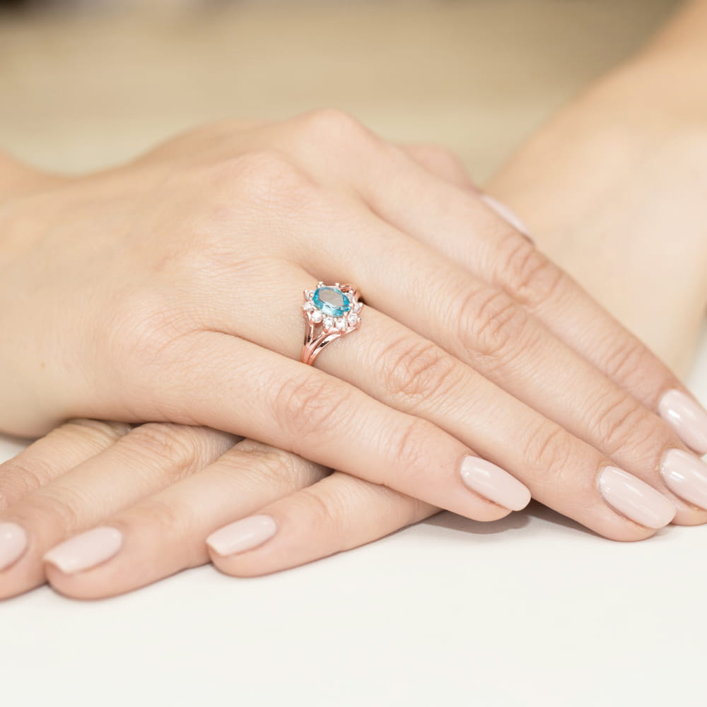 W0037.R3.TOB.01_4 Ręce z delikatnym manicure, na jednym palcu pierścionek z niebieskim kamieniem i ozdobnymi diamentami.