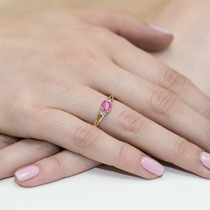 W0039.Z3.TOP.01_4 Złoty pierścionek z różowym kamieniem i diamentowymi zdobieniami na palcu z różowym manicure.