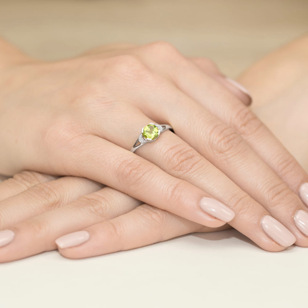 W0040.B3.PEG.01_4 Na dłoni znajduje się srebrny pierścionek z zielonym kamieniem, otoczony delikatnymi, zadbanymi paznokciami.