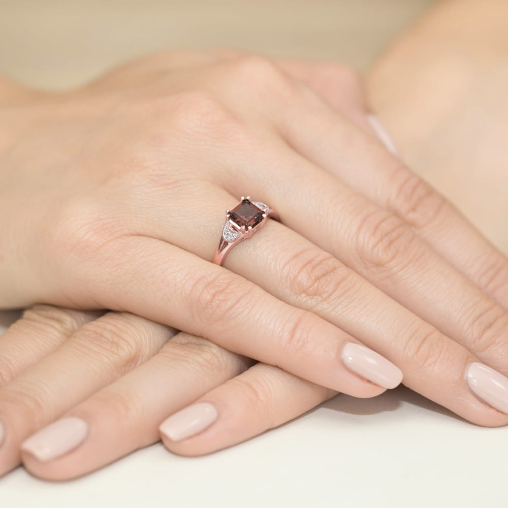 W0040.R3.GAR.02_4 Różowe złote pierścionek z ciemnym kamieniem na palcu, dłonie z zadbanymi paznokciami w neutralnym kolorze.