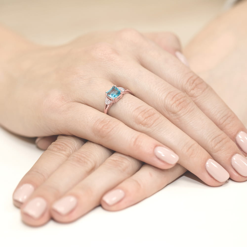 W0040.R3.TOB.02_4 Różowa pierścionek z niebieskim kamieniem na dłoniach z delikatnym manicure.