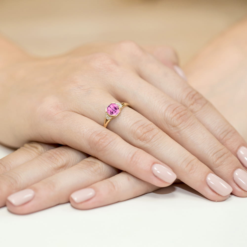 W0040.Z3.TOP.01_4 Złoty pierścionek z różowym kamieniem na palcu, dłonie z zadbanymi paznokciami.