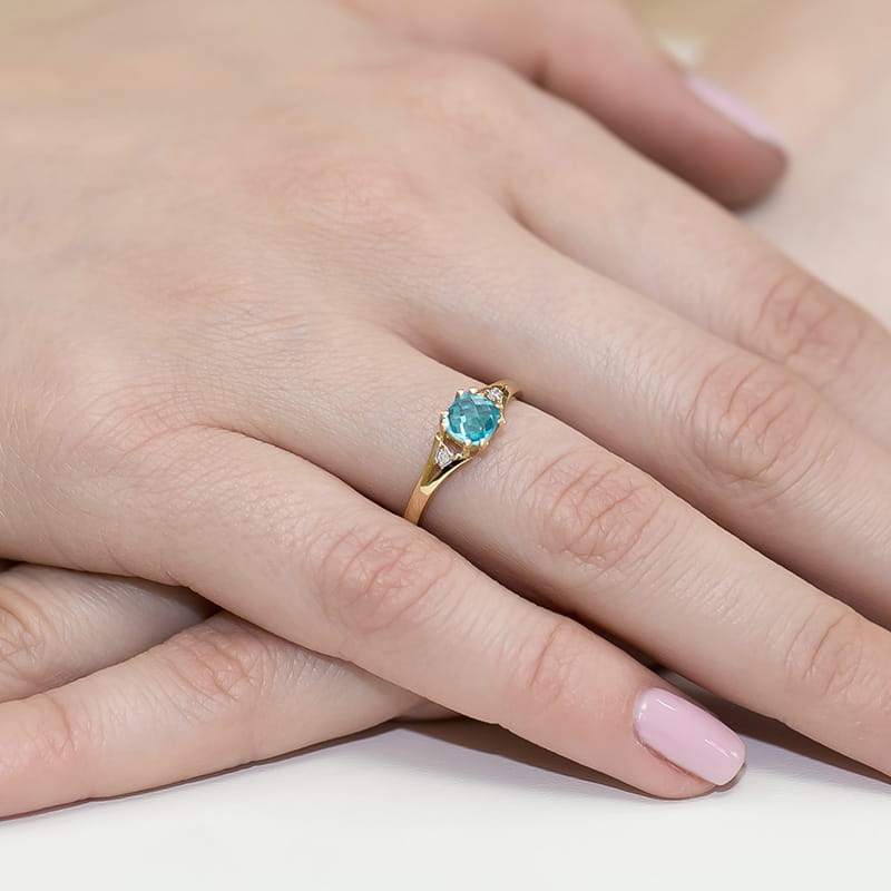 W0044.Z3.TOB.01_4 Złoty pierścionek z niebieskim kamieniem na palcu, dłonie z delikatnym manicure.