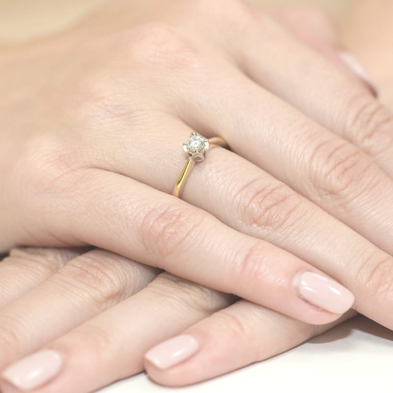 W0047.Z3.DIW.01_4 Zbliżenie na rękę z delikatnym złotym pierścionkiem z diamentem, na tle innych dłoni.