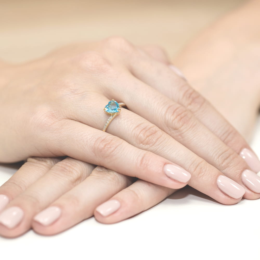 W0050.Z3.TOB.01_4 Złoty pierścionek z niebieskim kamieniem na palcu, dłonie z delikatnym manicure w jasnym kolorze.