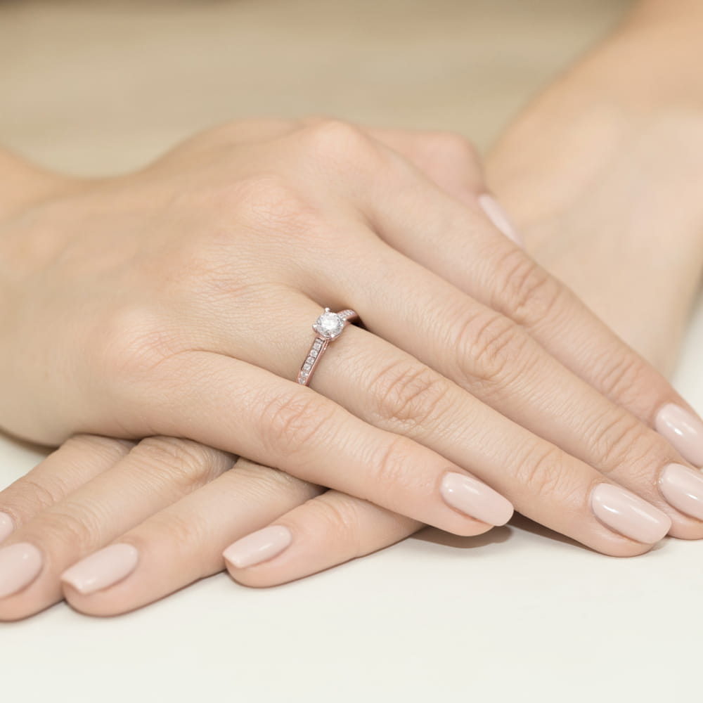W0052.R3.DIW.01_4 Na dłoni z delikatnym manicure znajduje się pierścionek z diamentem i małymi kamieniami.