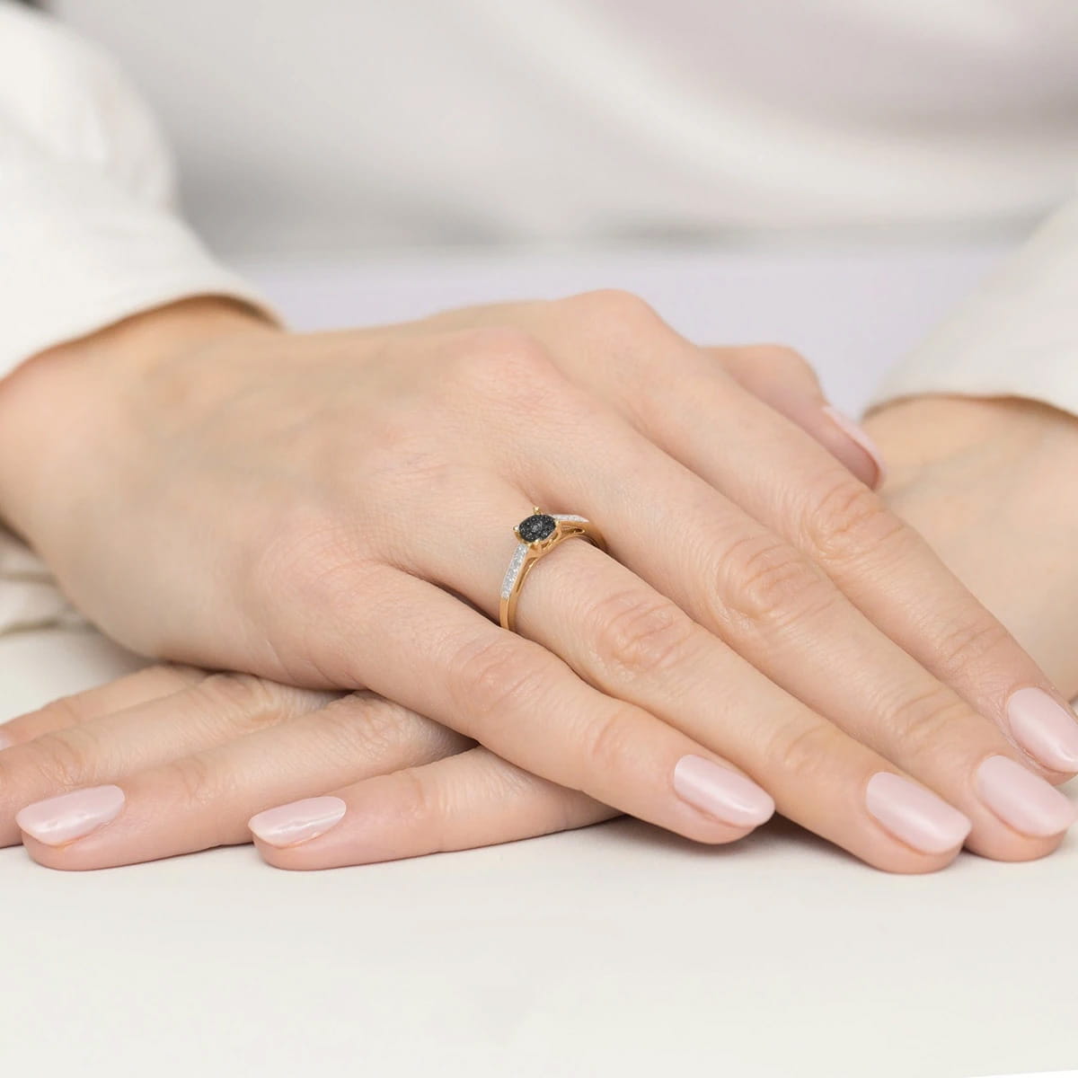 W0055.Z3.XXX.02_3 Złoty pierścionek z czarnym kamieniem na palcu, dłonie z delikatnym manicure w jasnym kolorze.