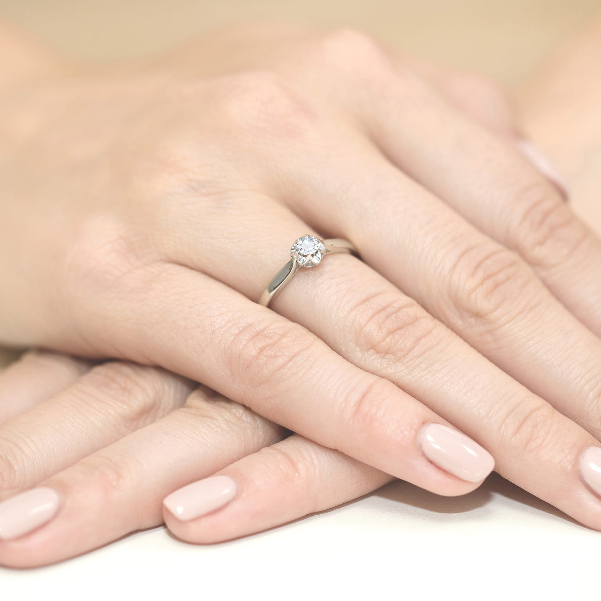 W0062.B3.LDW.01_4 Na dłoni widoczny pierścionek z dużym, błyszczącym diamentem, otoczony delikatnymi, zadbanymi palcami.