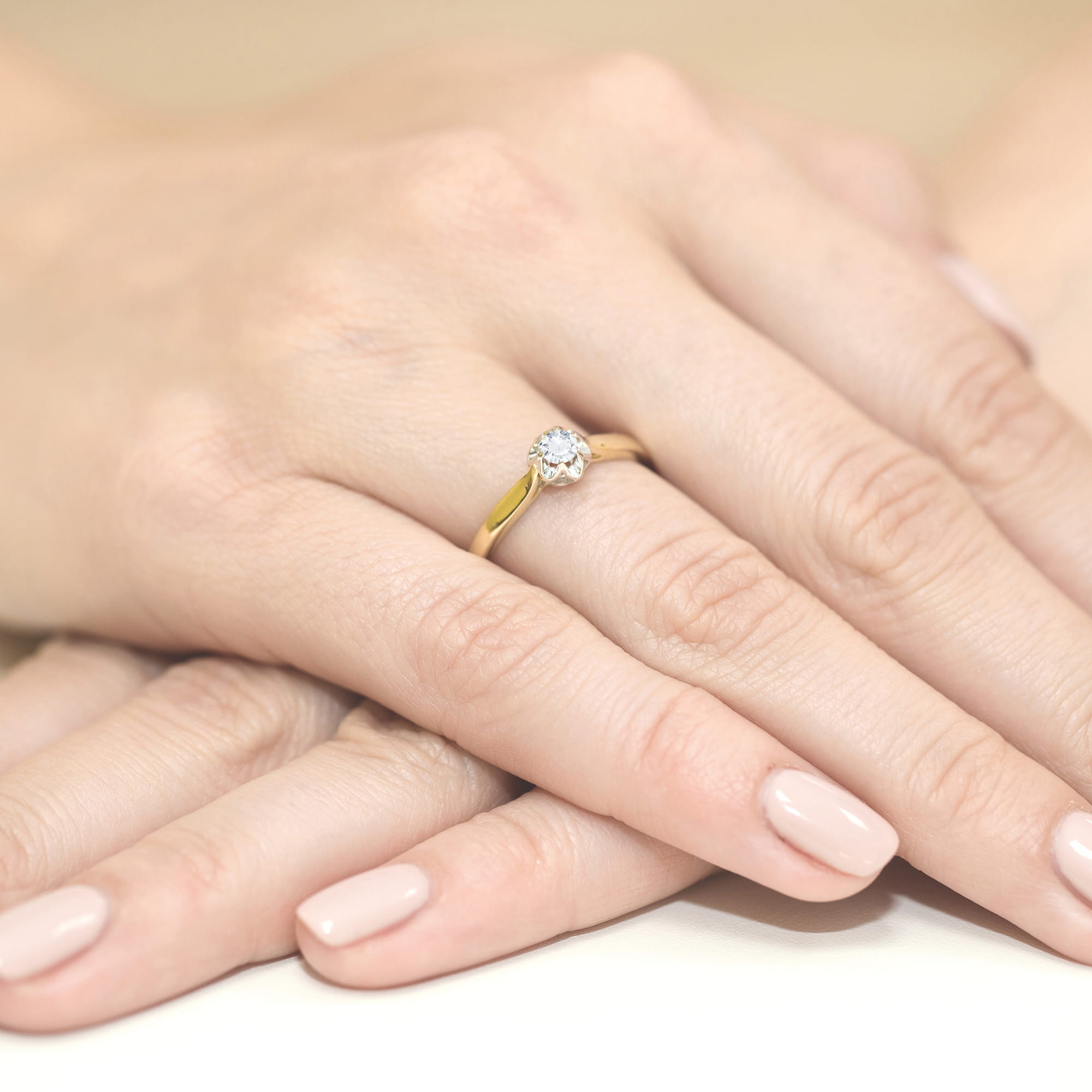 W0062.Z3.LDW.01_4 Złoty pierścionek z diamentem na palcu, dłonie z delikatnym manicure w jasnym kolorze.