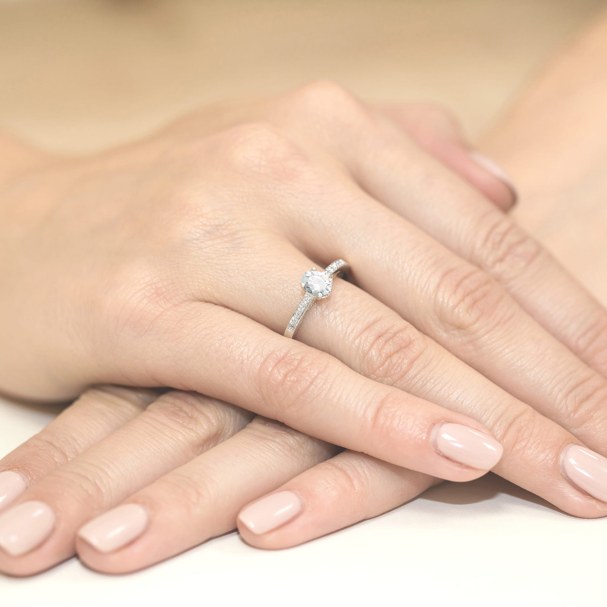 W0067.B3.LDW.01_3 Na dłoni z delikatnym manicure znajduje się pierścionek z dużym, błyszczącym kamieniem.