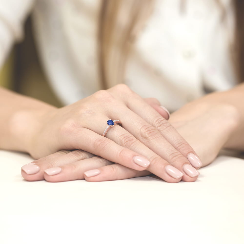 W0067.R3.SAB.01_3 Na dłoni z delikatnym manicure znajduje się pierścionek z niebieskim kamieniem.