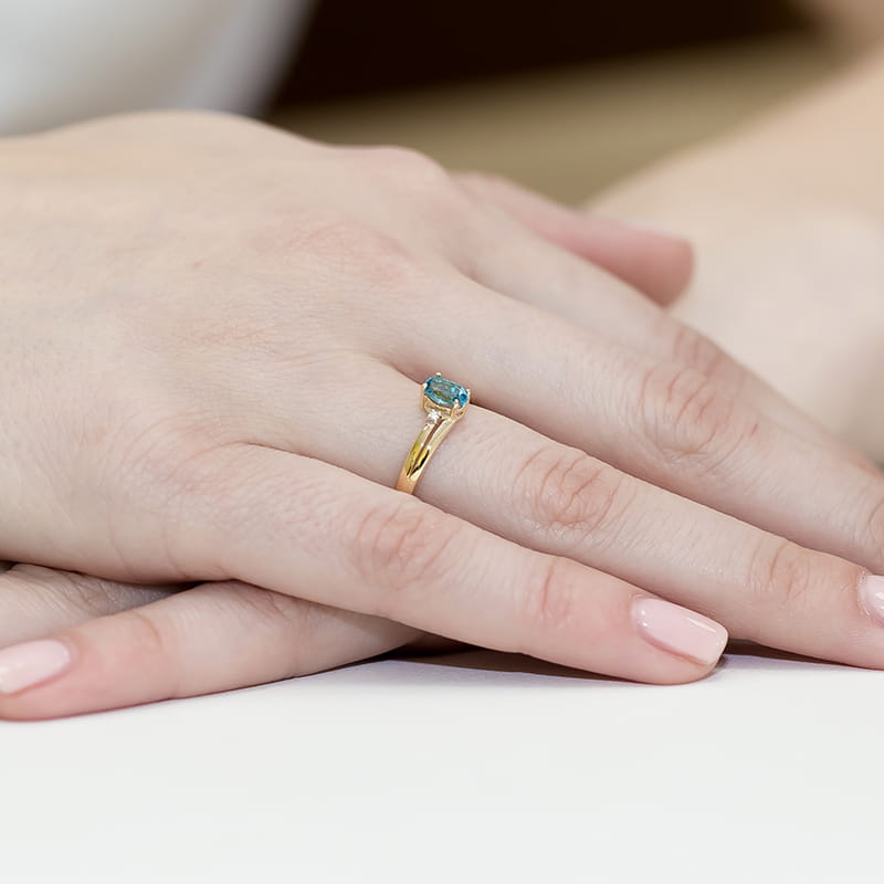 W0068.Z3.TOB.01_4 Złoty pierścionek z niebieskim kamieniem na palcu, dłonie z delikatnym manicure.