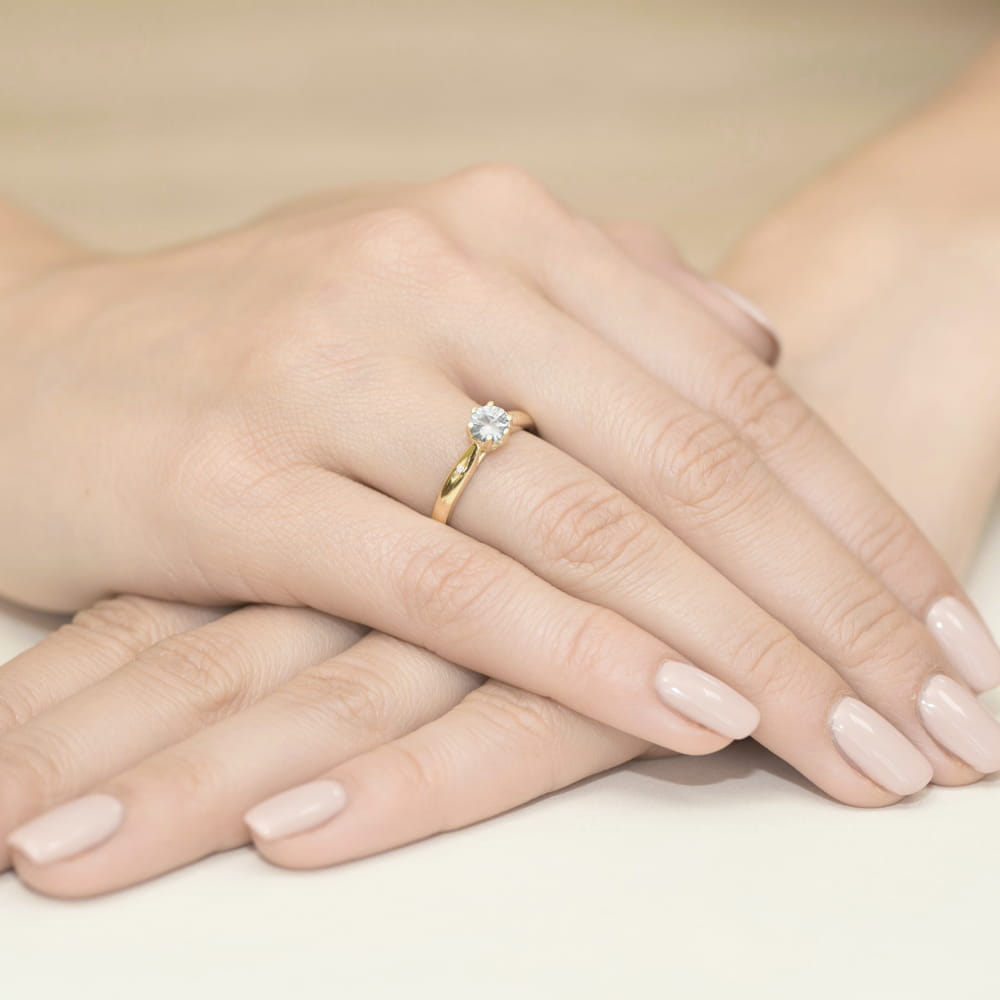 W0074.Z3.SW.01_4 Złoty pierścionek z diamentem na palcu, dłonie z delikatnym manicure w jasnym kolorze.