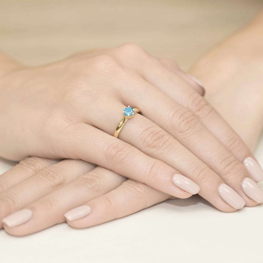 W0074.Z3.TOB.01_4 Złoty pierścionek z niebieskim kamieniem na palcu, dłonie z delikatnym manicure.