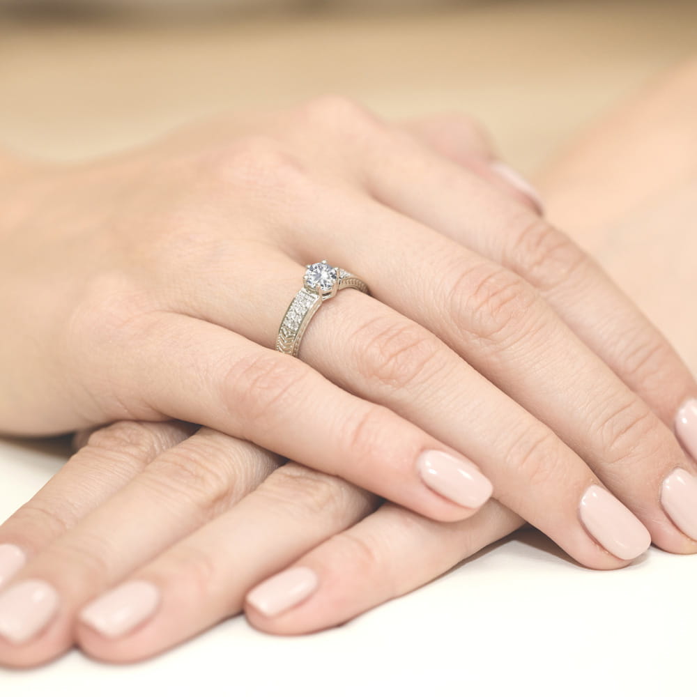 W0075.B3.SAW.01_4 Dwie dłonie z delikatnym manicure, jedna z pierścionkiem z dużym diamentem i ozdobnymi kamieniami.