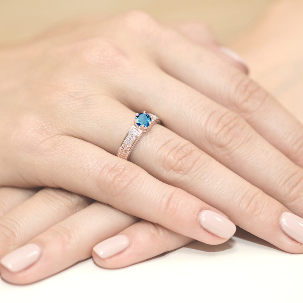 W0075.R3.TOL.01_4 Różowe złote pierścionek z niebieskim kamieniem, na dłoniach z delikatnym manicure.