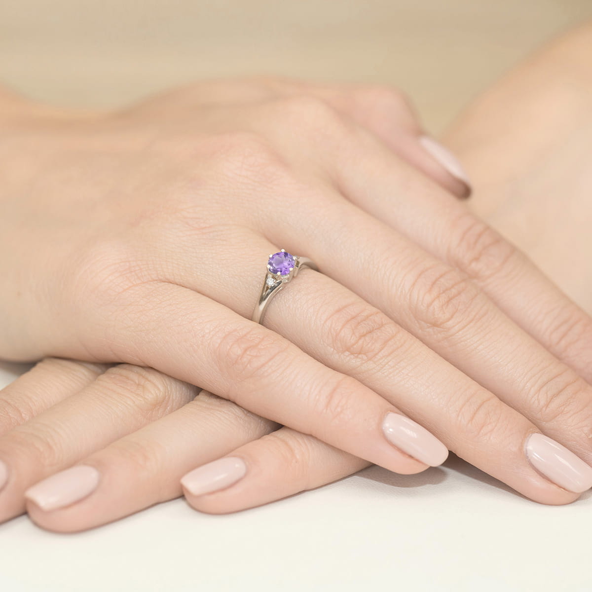 W0076.B3.AMV.01_4 Na dłoniach z delikatnym manicure znajduje się srebrny pierścionek z fioletowym kamieniem.