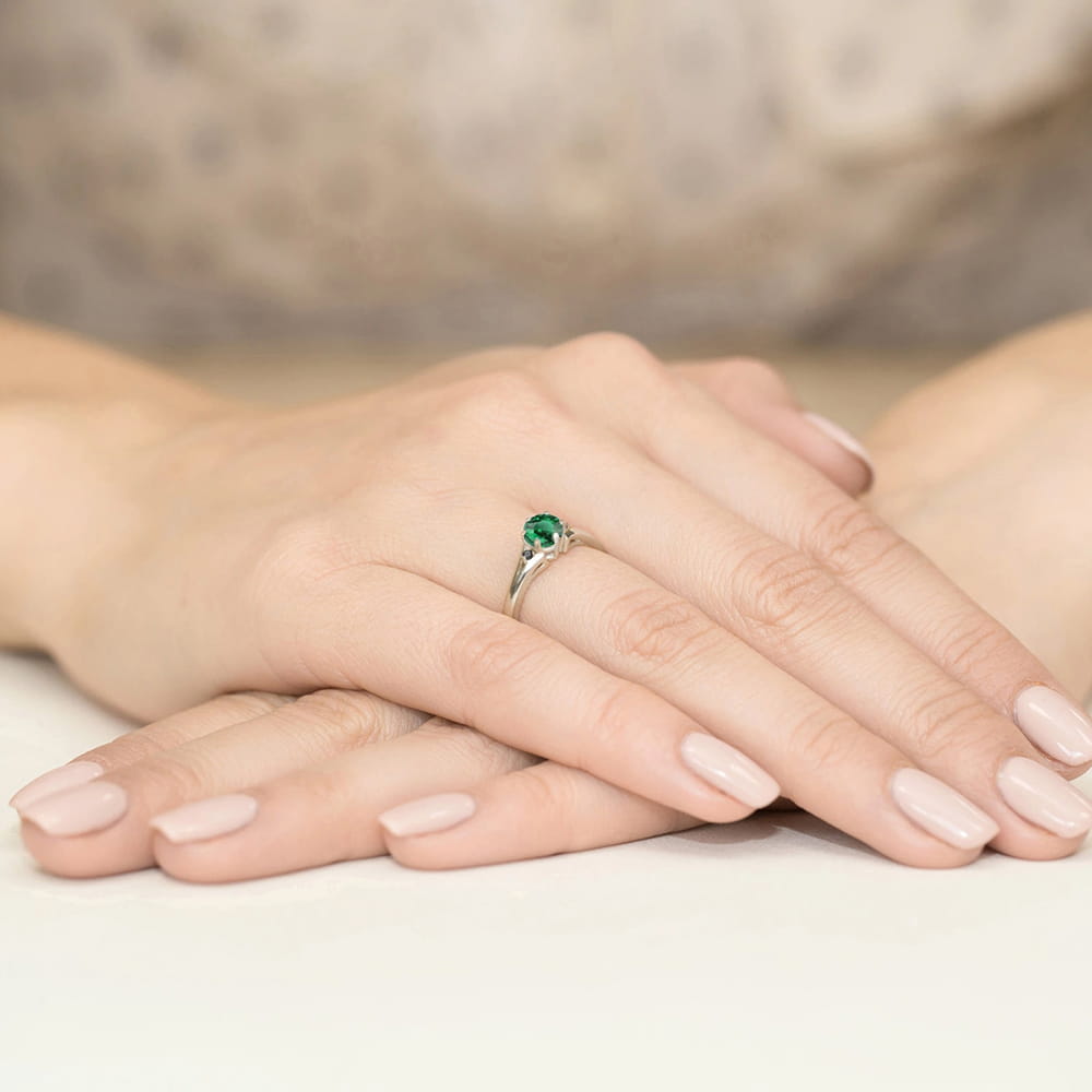 W0076.B3.EMG.02_3 Srebrny pierścionek z zielonym kamieniem na palcu, dłonie z delikatnym manicure w jasnym kolorze.