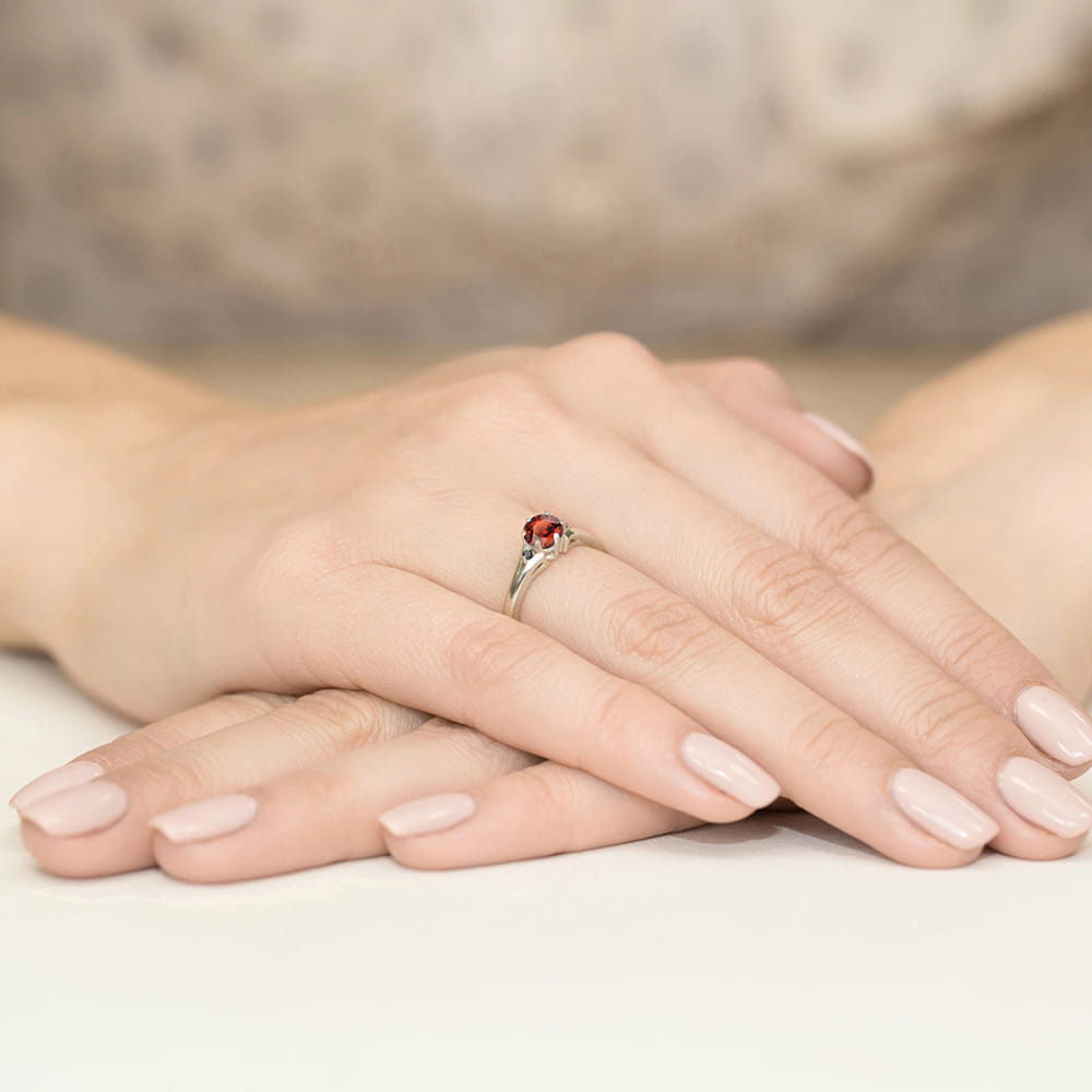 W0076.B3.GAR.02_3 Na dłoni z delikatnym manicure znajduje się srebrny pierścionek z czerwonym kamieniem.