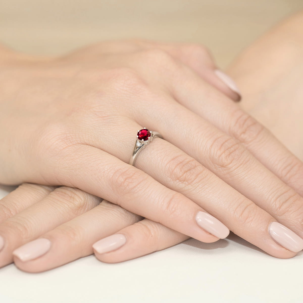 W0076.B3.RUR.01_4 Srebrny pierścionek z czerwonym kamieniem na dłoniach z delikatnym manicure.