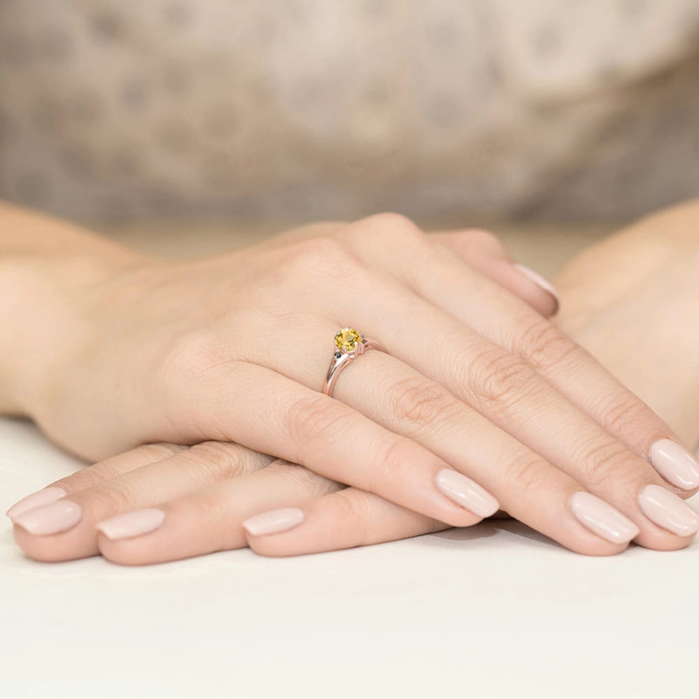 W0076.R3.CIY.02_3 Na dłoni z delikatnym manicure znajduje się srebrny pierścionek z żółtym kamieniem.