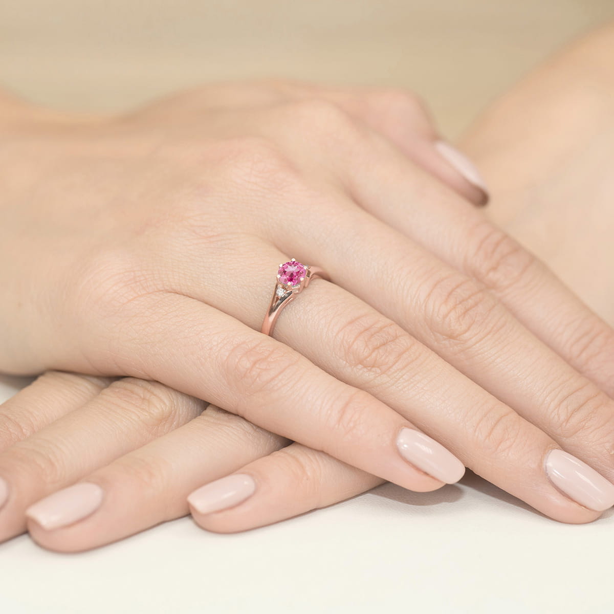 W0076.R3.TOP.01_4 Różowa pierścionek na palcu, dłonie z delikatnym manicure w neutralnym kolorze, ułożone na jasnym tle.