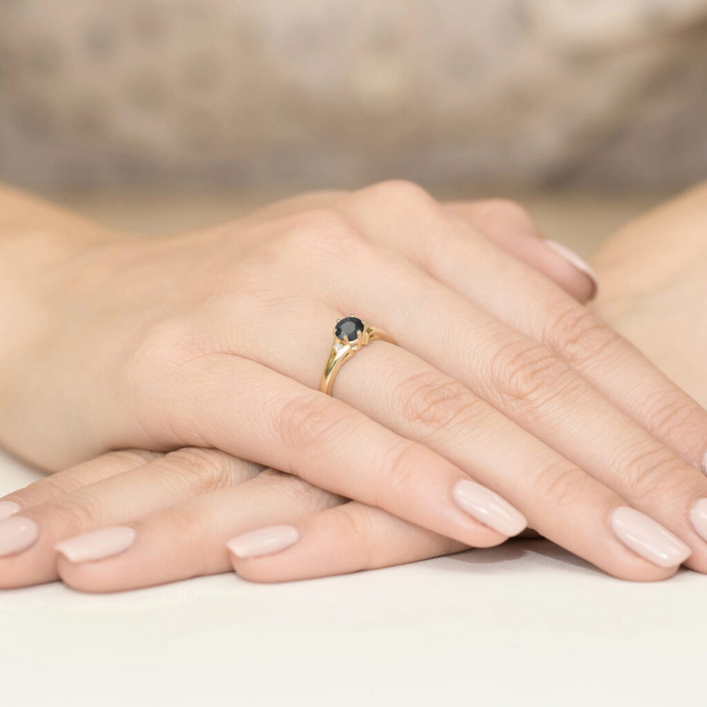 Złoty pierścionek z niebieskim kamieniem na palcu, dłonie z delikatnym manicure.