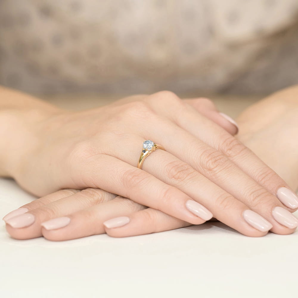 W0076.Z3.SAW.02_3 Złoty pierścionek z niebieskim kamieniem na dłoniach z delikatnym manicure w jasnym kolorze.