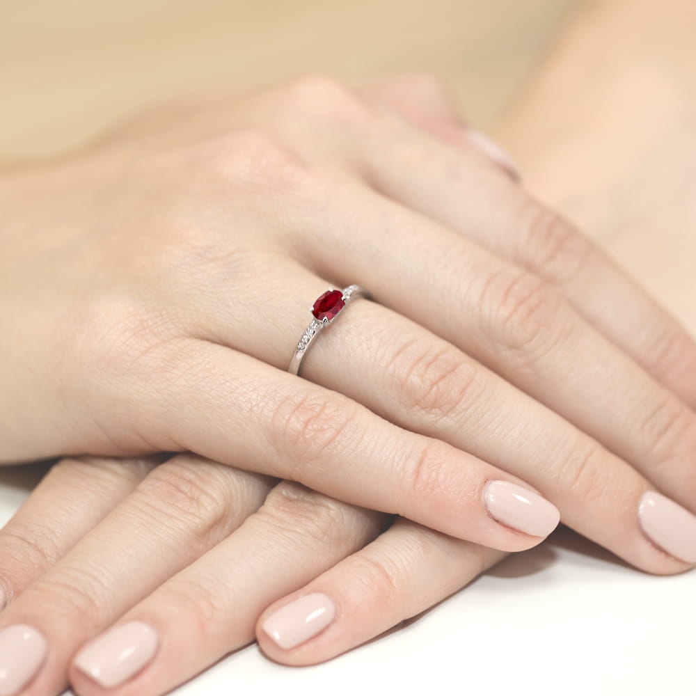 W0077.B3.RUR.01_4 Na dłoni widoczny jest srebrny pierścionek z czerwonym kamieniem i delikatnymi zdobieniami.