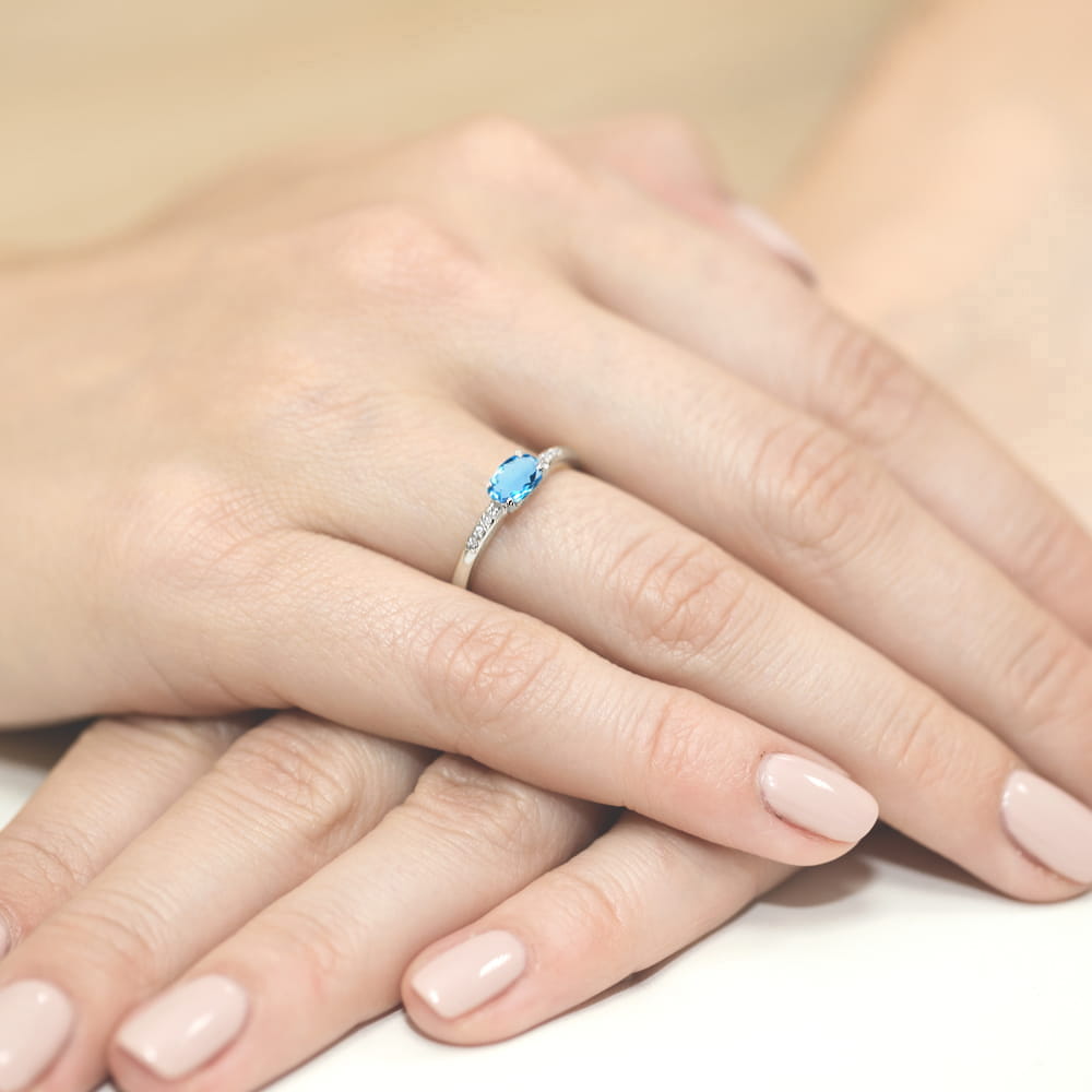 W0077.B3.TOB.01_4 Srebrny pierścionek z niebieskim kamieniem na dłoni z delikatnym manicure w odcieniu nude.