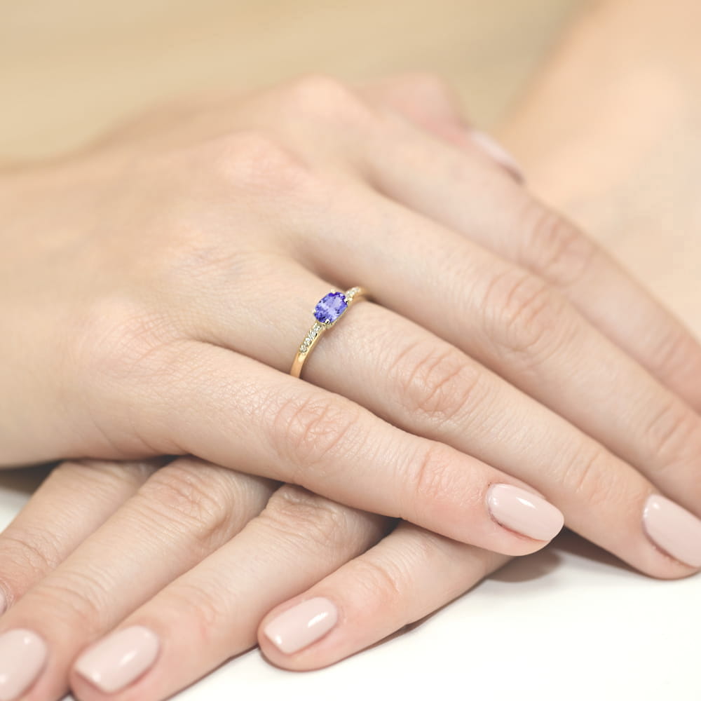 W0077.Z3.TAP.01_4 Złoty pierścionek z fioletowym kamieniem, na dłoniach z delikatnym manicure.