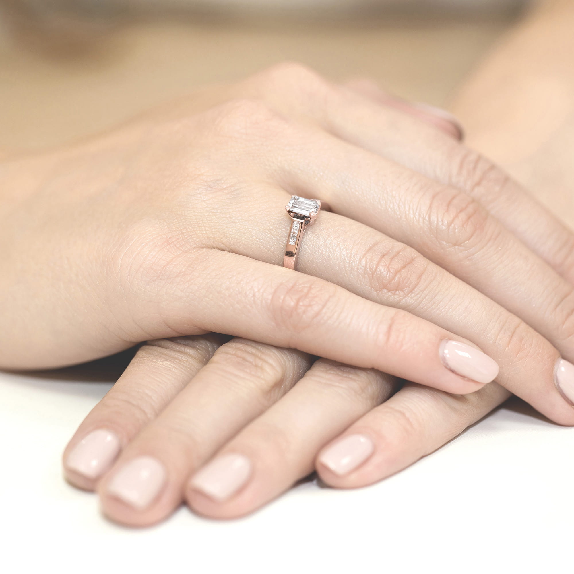 W0078.R3.LDW.01_4 Na dłoni znajduje się pierścionek z diamentem w kształcie prostokąta, otoczony delikatną obrączką.