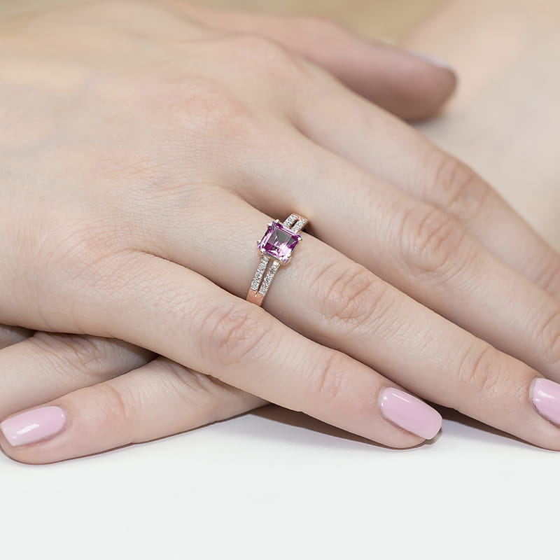 W0079.R3.TOP.01_4 Pierścionek z różowym kamieniem szlachetnym na palcu z delikatnymi, różowymi paznokciami.