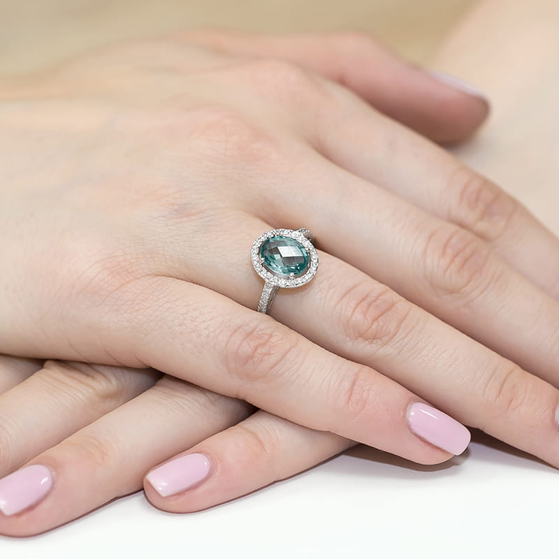 W0080.B3.TOB.01_4 Na dłoni z różowym manicure znajduje się srebrny pierścionek z dużym, owalnym kamieniem otoczonym diamentami.